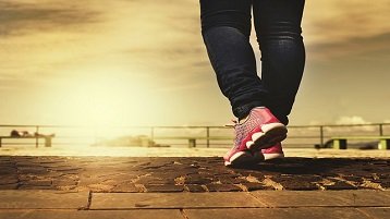 pernas de uma mulher com tenis rosa na calçada